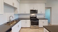Located at 3000 Van Buren Blvd in Riverside, California, this single-story residence offers a clean, contemporary design throughout. The open-concept kitchen serves as the heart of the home, showcasing white shaker cabinetry, dark countertops, a central island, and a full suite of stainless steel Whirlpool appliances including a gas range, microwave, and refrigerator. Light wood-look flooring runs throughout the main living and kitchen areas, lending warmth and continuity to the space. Recessed lighting and a ceiling fan contribute to a bright, comfortable atmosphere in the main area. The bedrooms feature plush carpeting, ceiling fans, and windows with blinds that invite natural light. Each bedroom is equipped with closet storage, including a walk-in closet with built-in shelving and hanging rods. The bathroom is finished with wood-look tile flooring, a full soaking tub with a curved shower rod, and clean white fixtures throughout. A dedicated in-unit laundry area houses a stacked Whirlpool washer and dryer, adding everyday convenience. The unit also includes an attached private garage with a sectional roll-up door and concrete flooring, providing secure parking and additional storage space.