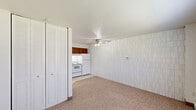 Located at 985 Wood Rd in Kenosha, Wisconsin, this efficient one-bedroom, one-bathroom unit offers a well-organized single-floor layout designed for practical, comfortable living. The open living area features neutral carpeting and white walls accented by a distinctive textured block-pattern wall, adding subtle character to the space. A ceiling fan with integrated lighting provides both airflow and illumination, while a window allows in natural light and outdoor views, complemented by baseboard heating along the perimeter. The entry area transitions seamlessly from tile flooring into the carpeted living space, creating a clean delineation at the front door. The kitchen is efficiently arranged with warm wood-toned cabinetry, white appliances including a range and refrigerator, and under-cabinet lighting that brightens the workspace. A double-door closet in the main living area offers generous storage. The bedroom is spacious relative to the overall footprint and continues the carpeted, light-toned aesthetic. The full bathroom is clean and well-appointed, featuring a white vanity with cabinet storage, a framed mirror with wall lighting, tile flooring, and a tiled shower-tub combination — all finished in a bright, neutral palette that enhances the sense of openness throughout.