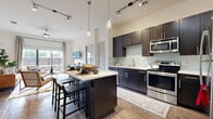 This single-floor residence offers two bedrooms, three bathrooms, and a thoughtfully designed layout that maximizes functionality and style. The open-concept kitchen serves as a central gathering space, featuring dark espresso cabinetry, light countertops, a subway tile backsplash, stainless steel appliances, and a freestanding island with bar seating. Track lighting and pendant fixtures illuminate the space, which flows naturally into the living area. Wood-look flooring runs throughout the main living spaces, adding warmth and continuity.

The living room receives abundant natural light through large sliding glass doors that open to a private outdoor patio, offering views of mature landscaping. The primary bedroom features plush carpeting, direct bathroom access, and a walk-in closet with built-in shelving and hanging storage. The second bedroom is generously sized with large windows and soft carpet. The bathrooms are finished with dark vanity cabinetry, light countertops, large-format tile flooring, and oversized mirrors. The overall ambiance is modern and cohesive, with a neutral palette and consistent design details throughout.