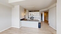 Unit 201R at 3450 W Clay St in Richmond, Virginia is a two-bedroom, one-bathroom residence offering a well-designed single-floor layout. The open-concept kitchen serves as a central feature, equipped with stainless steel appliances including a range, over-the-range microwave, and refrigerator. White shaker-style cabinetry pairs with dark granite countertops and a subway tile backsplash, while a peninsula with an integrated sink and pendant lighting above adds both function and visual interest. Light-toned hardwood-style flooring flows throughout the main living areas, complementing the neutral wall tones and track lighting.

The primary bedroom features carpeted flooring, a distinctive slatted ceiling detail, and dual sliding closets with built-in shelving, providing ample storage. The second bedroom also includes carpeted flooring and a spacious closet. A hallway connects the bedrooms to the shared full bathroom, which is appointed with a granite-topped double vanity, white cabinetry, a large mirror, tiled flooring with a marble-like finish, and a full tub-shower combination. The overall layout is efficient and cohesive, with a clean, contemporary aesthetic carried consistently throughout the unit.