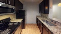 Located at 15610 Bellaire Ridge Dr in Charlotte, NC 28277, this single-floor residence offers a well-organized layout with a cohesive design throughout. The galley-style kitchen is a standout feature, boasting dark espresso cabinetry, granite countertops with a subtle tile backsplash, stainless steel appliances including a refrigerator and microwave, and light hardwood-style flooring that contributes to a warm, functional workspace. Adjacent to the kitchen, the open living and dining area is bathed in natural light from large windows dressed with horizontal blinds. Crown molding adds a refined touch, while a ceiling fan with pendant lighting provides both comfort and style. The hardwood-style flooring continues throughout this main living space, enhancing the sense of openness. The bedroom features plush wall-to-wall carpeting, a ceiling fan, and a closet with vertical blinds, creating a quiet and comfortable retreat. The bathroom is generously sized, offering a dual-sink vanity with dark cabinetry and a white countertop, a large mirror, and a combination soaking tub and shower with white tile surround. Hardwood-style flooring extends into the bathroom, maintaining visual consistency. The overall aesthetic is clean, neutral, and move-in ready.