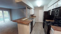 This single-floor unit offers a well-organized layout designed to maximize functionality across its one bedroom and one bathroom. The galley-style kitchen is a central feature, equipped with black appliances including a refrigerator, electric range, and built-in microwave. White cabinetry lines both sides of the kitchen, complemented by rich brown countertops and a stone tile backsplash that adds a decorative accent. Wood-look vinyl plank flooring runs throughout the kitchen, which connects seamlessly to the living area via a peninsula with additional counter seating.

The living area is carpeted and features crown molding, neutral gray walls, and a sliding glass door that introduces natural light and outdoor access. The open sightlines between the kitchen and living space create a cohesive, connected feel.

The bedroom is carpeted and includes crown molding, a ceiling fan with integrated lighting, and a window with blinds that allows for natural light. The bathroom features a full tub and shower combination with large-format gray tile surround accented by a mosaic tile border, wood-look flooring, and a grab bar for added convenience. Overall, the unit presents a clean, updated aesthetic with consistent finishes throughout.