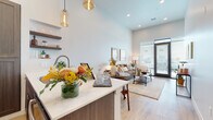 This thoughtfully designed single-floor residence offers a seamless blend of modern aesthetics and functional living. The open-concept layout connects the kitchen, dining, and living areas into one cohesive space, highlighted by soaring ceilings that amplify the sense of openness throughout.

The kitchen is outfitted with dark wood cabinetry, stainless steel appliances, a white quartz peninsula countertop with an undermount sink, and elegant amber glass pendant lighting. Floating wood shelves provide additional storage and display space, adding a warm, contemporary touch.

The dining area transitions naturally from the kitchen, offering an intimate setting adjacent to the main living space. The living room is bright and inviting, benefiting from large floor-to-ceiling windows and a glass patio door that floods the room with natural light and provides access to the outdoors.

The bedroom is generously proportioned with high ceilings, large windows dressed with layered curtains, and warm wood-look flooring that runs throughout the unit. A dedicated walk-in closet provides ample storage with built-in hanging rods and shelving.

The bathroom features rich dark wood vanity cabinetry with white countertops, a glass-enclosed tile shower, and warm wood-look flooring, creating a clean and polished finish. Overall, the space presents a warm, modern, and well-appointed living environment.