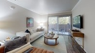 This single-story residence offers a thoughtfully designed layout with two bedrooms, two bathrooms, and a series of well-appointed living spaces. The living room serves as the centerpiece of the home, featuring crown molding, wood-style flooring, and a large sliding glass door that floods the space with natural light and opens onto a private balcony with tree-lined views. The open arrangement accommodates both lounge and entertainment areas comfortably.

The kitchen is outfitted with white shaker-style cabinetry, light quartz countertops, a stainless steel sink, and stainless steel appliances including a range and refrigerator. A window above the counter brings in additional natural light. Adjacent to the kitchen, the dining area provides a dedicated space for meals, with wood-style flooring and direct sightlines toward the hallway.

The primary bedroom features vaulted ceilings, a large window, and plush carpet, creating a calm retreat. The second bedroom is equally comfortable, with a bold design aesthetic, patterned carpet, and warm ambient lighting. The two bathrooms include a full bath with a tub-shower combination and white vanity, and a second bath with a walk-in tiled shower stall, both finished with wood-style flooring.