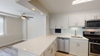 This single-floor unit features a clean, modern aesthetic carried consistently throughout its layout. The open-concept living area is bright and airy, benefiting from a wide bank of windows fitted with horizontal blinds that allow generous natural light to fill the space. Light wood-style luxury vinyl plank flooring runs throughout, lending warmth and visual continuity across all rooms. Ceiling fans are installed in both the living area and bedrooms, providing practical comfort.

The kitchen is thoughtfully designed with white shaker-style cabinetry, quartz countertops with subtle speckled detailing, and a light glass tile backsplash. Stainless steel appliances include a gas range, over-the-range microwave, dishwasher, and refrigerator. A peninsula counter separates the kitchen from the living area, offering additional prep space and a casual seating option.

The bedrooms are well-proportioned, featuring ceiling fans, neutral wall tones, and sliding-door closets with built-in shelving and hanging rods. The bathroom includes a tub-shower combination with white subway tile surround and a recessed mirrored medicine cabinet, maintaining the unit's clean, minimalist character throughout.