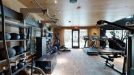 Located in New Braunfels, TX, this two-floor fitness facility offers a well-appointed exercise environment designed for a full range of workout experiences. The space is defined by its warm natural wood paneling and wood-plank ceilings, which lend a refined, contemporary aesthetic throughout both levels.

The upper floor serves as a dedicated studio-style exercise room featuring light hardwood flooring, large windows that frame views of the surrounding community, and wall-to-wall mirrors that amplify the sense of space and natural light. This level is equipped with cycling bikes, stability balls, rowing machines, and wall-mounted fans, making it ideal for cardio and functional fitness training. A mounted flat-screen display adds a multimedia element to workouts.

The lower floor transitions into a more traditional strength and conditioning space, featuring textured carpet flooring and a darker, high-contrast color palette with deep navy accent walls. This level houses a comprehensive array of equipment including cable machines, weight benches, a full dumbbell rack, treadmills, and additional cardio machines. Large mirrors line the walls to support proper form and technique. An open mezzanine-style railing connects both floors visually, reinforcing the facility's open and connected layout. Together, the two floors provide a complete, versatile fitness experience.