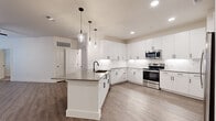 This well-appointed 2-bedroom, 2-bathroom single-floor residence offers a thoughtfully designed open-concept layout with contemporary finishes throughout. The kitchen serves as a central highlight, featuring crisp white shaker cabinetry extending to the ceiling, a marble-look tile backsplash, dark quartz countertops, and a full suite of stainless steel appliances including a side-by-side refrigerator with water and ice dispenser, a range, and a built-in microwave. A kitchen island with an undermount sink and pendant lighting above adds both function and style, while light wood-look flooring ties the kitchen and living area together seamlessly. The primary bedroom offers comfortable proportions, plush carpeting, a ceiling fan, and French doors that fill the room with natural light. It is complemented by a spacious walk-in closet with built-in shelving and a dedicated en-suite bathroom featuring a dual-sink vanity with gray quartz countertops, white cabinetry, and matte black hardware. The second bedroom also features carpeted flooring, a ceiling fan, and a natural light-filled window. Throughout the residence, clean white walls, recessed lighting, and consistent matte black fixtures create a cohesive, modern aesthetic.