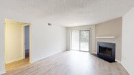 This single-floor residence offers a thoughtfully laid out living space with a variety of functional areas. The living room serves as the heart of the home, featuring light wood-style flooring, a textured ceiling, and a striking black-framed fireplace set against a warm-toned accent wall. A large sliding glass door with vertical blinds fills the room with natural light and provides a view of lush greenery outside.

Adjacent to the living area, the kitchen is well-appointed with rich wood cabinetry, granite-style countertops, and stainless steel appliances including a range and refrigerator. Light wood flooring continues throughout this space, and ample upper and lower cabinet storage makes it highly functional.

The bedrooms feature plush carpeting for added comfort, with at least one room offering direct outdoor access via a sliding glass door that opens to a balcony overlooking mature trees. Each bedroom includes closet space and benefits from natural light.

The bathroom is equipped with a full-size soaking tub and overhead shower with chrome fixtures, providing a clean and practical design. Throughout the residence, a neutral color palette of whites and soft beiges creates a bright, airy ambiance. Textured ceilings are consistent throughout, and the overall layout, as visible in the 3D overview, includes clearly defined living, kitchen, bedroom, and bathroom zones.