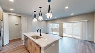 Located at 2080 FM 1102 in New Braunfels, TX, this thoughtfully designed 2-bedroom, 1-bathroom single-story unit offers a clean, modern aesthetic with high-quality finishes throughout. The open-concept kitchen and living area serves as the heart of the home, anchored by a striking central island with quartz countertops and an undermount sink, complemented by warm wood cabinetry, a marble-look tile backsplash, stainless steel appliances, and stylish globe pendant lighting. Recessed lighting and sliding glass doors in the living area invite abundant natural light and provide access to an outdoor balcony with exterior views. Wood-look plank flooring flows consistently throughout the entire unit, adding warmth and cohesion. Both bedrooms are well-proportioned, featuring ceiling fans, neutral wall tones, and ample natural light from windows with blinds. The bathroom is elegantly appointed with large-format tile flooring, a marble-style walk-in shower with matte black fixtures, and a wood-toned vanity. A dedicated laundry area houses a full-size washer and dryer with built-in shelving. Two closets and a hallway complete the efficient, well-organized layout of this contemporary New Braunfels residence.