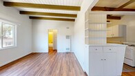 Located in Studio City, this 1-bedroom, 1-bathroom residence showcases a distinctive mid-century architectural character highlighted by prominent exposed wood beams spanning the white-paneled ceilings throughout. Rich hardwood flooring flows consistently across all rooms, lending warmth and cohesion to the entire space.

The open living room is bright and airy, benefiting from large windows that frame views of the surrounding hillside landscape and allow abundant natural light to fill the room. A wall-mounted A/C unit provides climate control. The living area connects seamlessly to the kitchen, which features white cabinetry with ample storage, a double-basin sink, light stone-toned countertops, and a gas range — all accented by the signature beamed ceiling overhead.

The bedroom offers a comfortable footprint with a sliding-door closet, continued hardwood flooring, and exposed beams, creating a consistent and cozy aesthetic. A ceiling fan in the adjoining area enhances ventilation and comfort.

The bathroom is cleanly appointed with tile surround walls in soft cream tones, a combination tub and shower with a handheld showerhead, a pedestal-style vanity, and a rectangular mirror. A hallway connects the principal rooms, completing the efficient and well-organized single-floor layout.