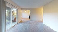 This single-floor unit offers a practical and well-organized layout, as illustrated by its detailed floor plan. The galley-style kitchen is a functional highlight, featuring white shaker cabinetry extending to the ceiling for ample storage, light-toned laminate countertops, black appliances including a refrigerator and electric range, a built-in dishwasher, and warm hardwood-style flooring that runs throughout the kitchen and entry areas. Overhead lighting keeps the space bright and well-illuminated.

The living area is generously sized with soft, neutral-toned carpeting underfoot and a ceiling fan overhead. A sliding glass door allows natural light to fill the room while providing outdoor views and access. The space flows openly into an adjacent area, enhancing the overall sense of roominess. A separate bedroom features the same plush carpeting and a baseboard heater, offering a quiet and comfortable retreat.

The full bathroom is clean and straightforward, with a tub and shower combination surrounded by classic white subway-style tile, a white vanity with cabinet storage beneath a light countertop, a wall-mounted mirror, and hardwood-style flooring that ties back to the kitchen. The overall aesthetic throughout is neutral and move-in ready.