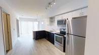 This well-designed 1-bedroom, 1-bathroom unit offers a smart and efficient single-floor layout that maximizes every square foot. The open-concept design seamlessly connects the kitchen and living area, creating a cohesive and functional living environment.

The kitchen is a standout feature, showcasing a striking two-tone design with sleek dark lower cabinets contrasted by bright white upper cabinetry. Stainless steel appliances — including a refrigerator, electric range, and over-the-range microwave — lend a polished, modern aesthetic. A clean white countertop runs along the peninsula, which doubles as a casual dining or prep surface. Pendant lighting and a track light fixture overhead add both style and practicality to the space.

Light hardwood-style flooring flows throughout, contributing warmth and continuity across the open layout. The living area benefits from natural light streaming in through large floor-to-ceiling window treatments, enhancing the bright and airy ambiance of the unit.

The overall design aesthetic is contemporary and clean, with a neutral color palette that provides a versatile backdrop for personalization. This unit is an excellent option for those seeking a modern, move-in-ready space with thoughtful design details throughout.