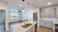 This well-appointed 2-bedroom, 2-bathroom single-floor residence offers a thoughtfully designed open-concept layout that maximizes functionality and comfort. The kitchen serves as a central hub, featuring a large granite-topped island with an undermount stainless steel sink, globe pendant lighting, soft gray shaker-style cabinetry, a marble-inspired tile backsplash, and a full suite of stainless steel appliances including a refrigerator and range. The kitchen flows seamlessly into the living area, which is bathed in natural light from multiple windows and accented by a ceiling fan. Wood-look flooring runs throughout the main living spaces, adding warmth and continuity. The primary bedroom offers plush carpeting, a ceiling fan, and direct access to a private en-suite bathroom. The en-suite features a granite vanity with an undermount sink, gray cabinetry with matte black hardware, and a large framed mirror. The second bedroom also features carpeted flooring, a ceiling fan, and a bright window with outdoor views. A second full bathroom mirrors the same refined finishes, complete with a granite vanity and a tub-shower combination with marble-style surround tile. Additional highlights include in-unit laundry and an additional room with wood-look flooring and abundant natural light.