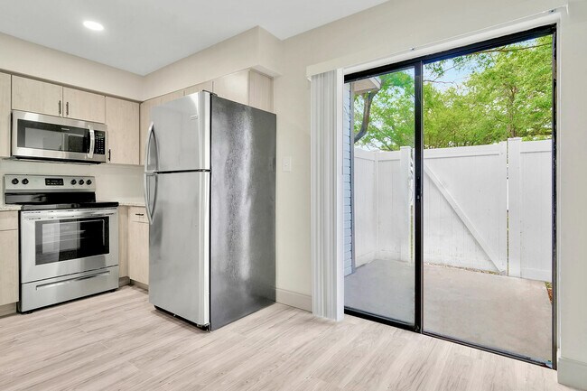 Cocina moderna y elegante con electrodomésticos de acero inoxidable y una puerta corrediza de vidrio brillante que conduce a un patio privado. - Temple Crest Townhomes