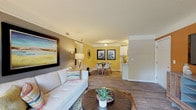 Located at 7113 Cape Harbor Dr in Wilmington, NC, this single-story residence offers a thoughtfully designed interior with a coastal-inspired aesthetic carried throughout. The open living area greets visitors with rich wood-look flooring, crown molding, and a striking burnt orange accent wall that anchors the space. A second living or flex area features a deep navy accent wall, adding a bold contrast to the neutral surroundings. The living and dining areas flow seamlessly together, with the dining space finished in warm golden-yellow tones and complemented by nautical wall art and a glass-top dining table. The kitchen is equipped with white shaker-style cabinetry, marble-look countertops, a double stainless steel sink, a dishwasher, and full-size black appliances. Two bedrooms provide comfortable retreats — the primary bedroom features soft gray and taupe tones with natural light from window blinds, while the secondary bedroom offers sage green accent walls and ample natural light. A full bathroom includes a soaking tub and shower combination. An in-unit laundry area houses a full-size washer and dryer, adding everyday convenience. Textured ceilings and consistent wood-look flooring tie the entire home together cohesively.