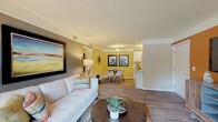 Located at 7113 Cape Harbor Dr in Wilmington, NC, this single-story residence offers a thoughtfully designed interior with a coastal-inspired aesthetic carried throughout. The open living area greets visitors with rich wood-look flooring, crown molding, and a striking burnt orange accent wall that anchors the space. A second living or flex area features a deep navy accent wall, adding a bold contrast to the neutral surroundings. The living and dining areas flow seamlessly together, with the dining space finished in warm golden-yellow tones and complemented by nautical wall art and a glass-top dining table. The kitchen is equipped with white shaker-style cabinetry, marble-look countertops, a double stainless steel sink, a dishwasher, and full-size black appliances. Two bedrooms provide comfortable retreats — the primary bedroom features soft gray and taupe tones with natural light from window blinds, while the secondary bedroom offers sage green accent walls and ample natural light. A full bathroom includes a soaking tub and shower combination. An in-unit laundry area houses a full-size washer and dryer, adding everyday convenience. Textured ceilings and consistent wood-look flooring tie the entire home together cohesively.