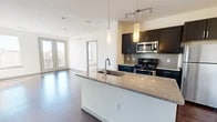 Located in Denver's vibrant Capitol Hill neighborhood, this well-appointed 2-bedroom, 2-bathroom residence offers a thoughtfully designed single-level layout. The open-concept living and kitchen area is anchored by rich hardwood flooring and an abundance of natural light streaming through large windows and French doors, which open to views of the surrounding cityscape. The kitchen is a functional centerpiece, featuring dark espresso cabinetry, a subway tile backsplash, stainless steel appliances, and a granite-topped island with an undermount sink and pendant lighting overhead. The living area connects seamlessly, making the space ideal for entertaining. Both bedrooms are carpeted for comfort and benefit from generous windows that frame urban views and fill the rooms with sunlight; a ceiling fan is present in the primary bedroom. The two bathrooms are finished with granite countertops, dark cabinetry with brushed hardware, and large mirrors. The primary bath includes a soaking tub and shower combination with tile surround and hardwood flooring. A dedicated closet and hallway complete the layout, offering practical storage. The overall aesthetic is clean, contemporary, and well-suited for urban living in Denver.