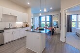 This contemporary single-floor residence at Nova at Queen Valley offers a thoughtfully designed open-concept layout with clean lines and modern finishes throughout. The expansive kitchen serves as the heart of the home, featuring crisp white cabinetry extending to the ceiling, dark quartz countertops, a classic subway tile backsplash, stainless steel appliances including a French door refrigerator and dishwasher, and a central island with pendant lighting overhead. Light wood-look flooring flows seamlessly from the kitchen into the dining area, where large windows and balcony access fill the space with natural light and outdoor views. The living area is bright and airy, with oversized windows framing scenic views of the surrounding landscape. The primary bedroom is a serene retreat featuring plush carpet, a ceiling fan, large windows, and ample natural light. A generously sized walk-in closet with wire shelving provides abundant storage. The bathroom is clean and functional, finished with light flooring, a walk-in shower, and a vanity with a dark countertop. An additional bedroom offers comfortable accommodations with recessed lighting and window views. Throughout the residence, neutral tones, recessed lighting, and high ceilings create a bright, welcoming ambiance.