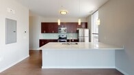 Located at 3219 Detroit Ave in Cleveland's vibrant Ohio City neighborhood, this single-floor residence offers a thoughtfully designed open-concept layout with contemporary finishes throughout. Rich hardwood-style flooring flows seamlessly across the living and sleeping areas, complemented by exposed concrete ceilings and crisp white walls that lend an urban, loft-inspired character to the space.

The expansive living area is bathed in natural light through large floor-to-ceiling sliding glass doors and multiple double-hung windows, offering views of the surrounding neighborhood and access to an outdoor area. A barn-style sliding door adds an architectural detail that balances industrial and modern aesthetics.

The kitchen is a standout feature, boasting rich dark mahogany cabinetry, a soft green subway tile backsplash, and a full suite of stainless steel appliances including a range, microwave, and refrigerator. A generous white quartz island with a double sink serves as both a functional workspace and a social centerpiece, illuminated by elegant pendant lighting.

The bedroom is quietly set apart, offering natural light via a window and closet access. The bathroom is finished with large-format linear tile in the walk-in shower, a dark vanity with a quartz countertop, and light wood-tone flooring, creating a clean and modern retreat.