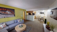 Located at 3040 E Shea Blvd in Phoenix, AZ, this single-floor unit offers a thoughtfully designed open-concept layout that connects the living, dining, and kitchen areas into one cohesive space. The living room features plush carpeting, a bold chartreuse accent wall, and a wall-mounted TV, creating a comfortable and stylish gathering area. The kitchen is equipped with light wood cabinetry, black appliances including a range and microwave, and a peninsula that provides a natural divider between the kitchen and living space. A dedicated dining area sits adjacent, complete with a mirror that adds depth to the room. The bedrooms are well-appointed, each featuring carpet flooring, large windows with vertical blinds, and vibrant accent walls in shades of teal and sage green that lend each room a distinctive character. One bedroom includes a cozy seating nook, ideal for use as a reading or lounging area. The unit includes two full bathrooms, each with a tub-shower combination, vanity with ample counter space, and a large mirror. Textured ceilings are consistent throughout the unit. The overall ambiance is colorful, functional, and inviting, reflecting a well-maintained residential space in the heart of Phoenix.
