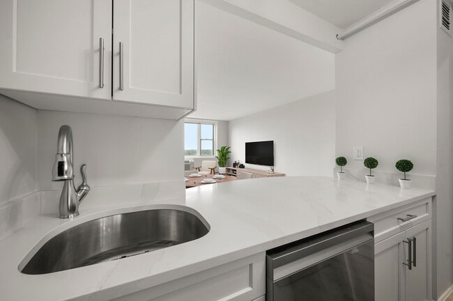 Modern kitchen with sleek stainless-steel appliances, statuario quartz countertops, and six burner gas stove, opening into a bright living area with a large window view at Parkside Place, apartments in Cambridge, MA - Parkside Place Apartments