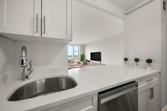 Modern kitchen with sleek stainless-steel appliances, statuario quartz countertops, and six burner gas stove, opening into a bright living area with a large window view at Parkside Place, apartments in Cambridge, MA - Parkside Place