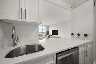 Modern kitchen with sleek stainless-steel appliances, statuario quartz countertops, and six burner gas stove, opening into a bright living area with a large window view at Parkside Place, apartments in Cambridge, MA - Parkside Place