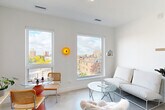 Located at 3740 Second Ave in Detroit's vibrant Midtown neighborhood, this efficiently designed unit offers a thoughtfully organized single-floor layout. The bright living area serves as the heart of the space, featuring crisp white walls, polished concrete floors, and large windows that frame elevated views of the surrounding Detroit cityscape, flooding the room with abundant natural light. A galley-style kitchen runs parallel to the main living area and is outfitted with light wood cabinetry, open metal shelving, a stainless steel sink, full-size refrigerator, and modern appliances — combining both functionality and clean, contemporary aesthetics. The sleeping area is tucked into a private nook, offering a quiet and minimalist retreat with an all-white interior. The bathroom features subway-tiled shower walls and a clean, modern finish. Additional practical features include a dedicated closet for storage and an in-unit laundry area. Throughout the space, the consistent use of white walls, concrete flooring, and natural wood tones creates a cohesive modern aesthetic. The unit's elevated position provides pleasant views over the neighboring Midtown rooftops and greenery, enhancing the overall sense of openness despite the compact footprint.