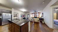 This 2-bedroom, 3-bathroom residence is designed with an open-concept floor plan that seamlessly connects the kitchen, dining, and living areas. Rich hardwood flooring flows throughout the main living spaces, complemented by neutral wall tones that create a bright and welcoming atmosphere. The kitchen is well-equipped with dark espresso cabinetry, dark granite countertops, stainless steel appliances including a range, microwave, and refrigerator, and a classic subway tile backsplash. A kitchen island with an integrated sink adds both functionality and workspace. The dining area comfortably accommodates a full dining table and is adjacent to the living room, which features a ceiling fan and large windows dressed with bold accent curtains that invite ample natural light. The primary bedroom includes carpeted flooring, a ceiling fan, a natural light-filled window, and direct access to a dedicated walk-in closet with wire shelving. The second bedroom also features carpet and a window with outdoor views. The bathrooms are finished with hardwood-style flooring, dark wood vanities, and glass-enclosed showers. Two closets provide generous storage throughout. A hallway connects the private quarters, completing this efficiently designed and well-finished residence.