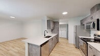 Located at 5799 Trail Ave NE in Keizer, Oregon, this well-appointed 2-bedroom, 2-bathroom single-floor unit offers a clean, modern aesthetic throughout. Light-toned hardwood-style flooring runs continuously across the entire space, creating a cohesive and bright atmosphere.

The heart of the unit is the open-concept kitchen, which features striking concrete-finish cabinetry with matte black hardware, white quartz countertops, an undermount sink with a sleek black faucet, and stainless steel appliances including a refrigerator, range, microwave, and dishwasher. The galley-style kitchen flows seamlessly into the dining and living areas, where natural light filters in through windows with views of surrounding greenery.

A dedicated in-unit laundry area with a washer and dryer is conveniently accessible from the kitchen corridor. Three closets provide generous storage throughout the unit.

Both bedrooms are bright and inviting, with large windows allowing ample natural light, and the primary bedroom offers a comfortable and well-proportioned layout. Each bathroom is finished with white vanities, white quartz countertops, framed mirrors, and chrome fixtures, conveying a clean and contemporary feel.

The entrance provides a welcoming transition into the space, and the overall design emphasizes functionality and modern simplicity throughout.
