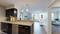 The Bowie's Innova floor plan is a thoughtfully designed one-bedroom, one-bathroom residence that balances modern style with functional living. The open-concept layout seamlessly connects the kitchen and living area, creating a welcoming and versatile space. The kitchen features dark espresso cabinetry, granite countertops, stainless steel appliances, a built-in dishwasher, and pendant lighting above the peninsula, which also serves as a casual dining or prep area. Light wood-style flooring flows throughout the main living space, enhancing the airy feel. The living room is generously proportioned, bathed in natural light from large windows with views of surrounding greenery, offering a bright and relaxing atmosphere. The bedroom is carpeted for comfort and includes ample space for a full furniture arrangement, a window for natural light, and direct access to the bathroom. The bathroom is elegantly finished with large-format tile flooring, a dark vanity with granite countertops, a wide mirror with sconce lighting, and a clean, modern aesthetic throughout. This residence offers a cohesive design palette of neutral tones, quality finishes, and practical features that make it an ideal modern living space.