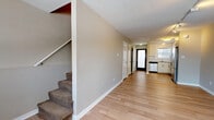 Located at 2000 Walnut St in Boulder, Colorado, this two-story residence offers a well-organized layout spread across two floors connected by a carpeted staircase. The main level features an open living area with light wood-style flooring, neutral-toned walls, and track lighting that enhances brightness throughout. A hallway leads from the living space toward the entry door and the kitchen, which is efficiently designed with crisp white cabinetry, a white tile backsplash, a stainless steel refrigerator, range with microwave, and dishwasher — all contributing to a clean, functional aesthetic. Natural light enters through a window above the kitchen sink, adding warmth to the space. A separate living or dining area on the main level also benefits from track lighting and a row of windows offering exterior views. The bedrooms are carpeted and spacious, each featuring large windows that bring in natural light and baseboard heating units for year-round comfort. The bathroom is finished with large-format tile flooring, a full bathtub with a white subway-tiled surround, and a sliding glass enclosure, presenting a clean and classic design. Throughout the residence, the combination of wood-style flooring on the main level and plush carpet upstairs creates a practical and comfortable living environment suited for Boulder's dynamic lifestyle.