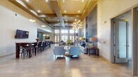 Located at 2707 Showplace Dr in Naperville, IL, this single-floor clubhouse-style space is designed with an upscale, contemporary aesthetic that balances comfort and functionality. The main lounge area commands attention with dramatically tall ceilings accented by coffered details and bold sputnik-style chandeliers that cast warm, ambient light across the expansive open floor plan. Large-format tile flooring flows throughout, lending a cohesive, polished look to the entire space.

The lounge features multiple seating arrangements, including tufted sofas, accent chairs, and occasional tables grouped around a striking floor-to-ceiling textured slate feature wall. A classic stone-mantled fireplace anchors one end of the room, accompanied by a wall-mounted flat-screen TV and flanked by tall windows and glass French doors that flood the space with natural light and provide access to an outdoor terrace.

A dedicated kitchen bar area showcases a long quartz-topped island with warm wood bar stools, dark cabinetry, and a vibrant mosaic tile backsplash in cool blue tones. Pendant lighting and an additional mounted TV complete this functional gathering space. Nearby, a high-top dining table with rich wood tones offers a more intimate setting, while a glass-paned interior door provides access to a private meeting or office area, rounding out this well-appointed communal facility.