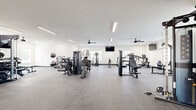Located at 195 Eddings Rd in Franklin, Kentucky, this fitness center offers a generously sized, single-floor exercise space designed to support a wide range of workout routines. The facility features a clean, modern aesthetic with crisp white walls, durable rubber-speckle flooring, and bright linear lighting that ensures excellent visibility throughout.

The space is thoughtfully organized into distinct workout zones. The cardio area is equipped with treadmills, elliptical machines, and a recumbent bike, complemented by a wall-mounted television and ceiling fans that help maintain a comfortable environment during exercise. A dedicated strength training section features multiple cable machines, a multi-function weight station, a dumbbell rack with a full range of free weights, and adjustable benches to accommodate a variety of exercises.

Natural light filters in through multiple windows fitted with blinds, offering views of the surrounding outdoor areas, including a glimpse of a pool. A set of glass-panel French doors provides an additional exit and further brightens the space. The layout allows for ample open floor space, making it suitable for stretching, functional training, or group exercise. Ceiling fans distributed throughout the room contribute to airflow and overall comfort, making this a practical and well-appointed fitness facility.