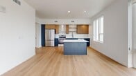 Located in the heart of Salt Lake City, this well-appointed 1-bedroom, 2-bathroom unit offers a thoughtfully designed open-concept layout bathed in natural light. The combined living, dining, and kitchen area serves as the centerpiece of the home, featuring light hardwood flooring, shiplap ceilings with recessed lighting, and dramatic floor-to-ceiling windows that frame sweeping views of the city skyline and surrounding mountains. A sliding glass door leads to a private balcony, extending the living space outdoors. The kitchen is a standout, showcasing a large center island with white quartz countertops, two-tone cabinetry in warm wood and navy blue, subway tile backsplash, and stainless steel appliances. The spacious primary bedroom is finished with plush carpet, a ceiling fan, shiplap ceiling detail, and a charming barn door entry leading to a generous walk-in closet with built-in shelving and hanging rods. The primary bathroom is sleek and modern, with a dual-sink vanity featuring wood cabinetry, white countertops, and a clean walk-in shower. A second full bathroom and dedicated utility room round out this efficient, contemporary home.