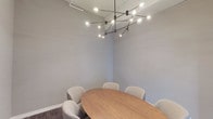 This contemporary single-floor commercial space is thoughtfully designed to support a productive and professional work environment. Entry is made through sleek full-height glass doors framed in matte black, immediately establishing a tone of modern sophistication. The open-plan interior is anchored by durable wood-look flooring that flows seamlessly throughout, complemented by a clean white drop ceiling with recessed lighting.

Glass-partitioned offices and meeting areas line the space, maximizing transparency and natural light while maintaining acoustic separation. A dedicated conference room features an oval wood table surrounded by upholstered boucle chairs, all illuminated by a striking multi-arm sputnik-style chandelier that serves as a bold focal point.

A comfortable lounge and breakout area is highlighted by a linear gas fireplace set against a dramatic stacked-stone accent wall. Large picture windows flood this zone with natural light and provide street-facing views, making it ideal for informal meetings or relaxation. Pendant lighting in warm gold tones adds an inviting ambiance overhead.

The kitchenette is well-appointed with rich dark cabinetry, light stone countertops, a stainless steel side-by-side refrigerator with water and ice dispenser, a sink, and a coffee station—providing convenient amenities for daily use. A corridor leads to additional private offices and support spaces, completing this polished and functional commercial layout.