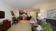 Located at 11077 W Forest Home Ave in Hales Corners, Wisconsin, this single-floor residence offers a thoughtfully designed open-concept layout that seamlessly connects the kitchen, dining, and living areas. The kitchen is a standout feature, showcasing rich cherry wood cabinetry, granite countertops, stainless steel appliances including a refrigerator, range, and built-in microwave, and wood-look tile flooring. A center island with pendant lighting provides additional prep space and casual seating. The dining area sits adjacent to the kitchen, while the living room extends naturally from this central hub, offering plush carpeting and a large sliding glass door dressed with vertical blinds that allows generous natural light to fill the space. A dedicated media area with wall-mounted television and additional seating rounds out the living space. The bedroom is a serene retreat with soft carpeting, neutral tones, and a window that brings in natural light. A full bathroom with light tile flooring completes the layout, accessible via a private hallway. Throughout the residence, a cohesive neutral color palette, warm wood accents, and quality finishes create an inviting and functional living environment.