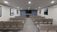 Located at 500 Harry S Truman Dr in Largo, Maryland, this single-floor screening room offers a cozy, cinema-inspired environment designed for group viewing and entertainment. The room is outfitted with multiple rows of cushioned, theater-style chairs in a soft blue-gray upholstery, arranged to provide clear sightlines to a wall-mounted flat-screen display at the front of the room. The front accent wall is painted in a muted steel blue, creating a focal point that anchors the space and adds a touch of cinematic atmosphere.

The walls are adorned with a curated selection of framed vintage movie posters, including classic titles such as "The African Queen," "2001: A Space Odyssey," "Rio Grande," "Forrest Gump," and "The Wizard of Oz," lending the room a nostalgic, film-enthusiast character. Recessed lighting throughout the ceiling provides even, adjustable illumination suited for both pre-show gatherings and screenings.

A standout feature is the classic red-and-gold popcorn cart stationed in the corner, adding a genuine movie-house charm to the experience. A decorative wood-and-glass media console provides additional storage and display space. Patterned, neutral-toned carpet completes the room's welcoming and functional design, making this screening room an engaging communal amenity.