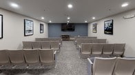 Located at 500 Harry S Truman Dr in Largo, Maryland, this single-floor screening room offers a cozy, cinema-inspired environment designed for group viewing and entertainment. The room is outfitted with multiple rows of cushioned, theater-style chairs in a soft blue-gray upholstery, arranged to provide clear sightlines to a wall-mounted flat-screen display at the front of the room. The front accent wall is painted in a muted steel blue, creating a focal point that anchors the space and adds a touch of cinematic atmosphere.

The walls are adorned with a curated selection of framed vintage movie posters, including classic titles such as "The African Queen," "2001: A Space Odyssey," "Rio Grande," "Forrest Gump," and "The Wizard of Oz," lending the room a nostalgic, film-enthusiast character. Recessed lighting throughout the ceiling provides even, adjustable illumination suited for both pre-show gatherings and screenings.

A standout feature is the classic red-and-gold popcorn cart stationed in the corner, adding a genuine movie-house charm to the experience. A decorative wood-and-glass media console provides additional storage and display space. Patterned, neutral-toned carpet completes the room's welcoming and functional design, making this screening room an engaging communal amenity.