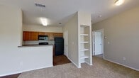 This single-floor residence offers a functional and well-organized layout designed for comfortable everyday living. The kitchen is equipped with warm-toned wood cabinetry, dark granite-style countertops, and black appliances including a refrigerator, electric range, and over-the-range microwave. Durable wood-look flooring runs throughout the kitchen area, providing a clean contrast to the plush carpeting found in the living and bedroom spaces. A peninsula counter separates the kitchen from the open living area, which features a built-in set of white display shelves — a practical and decorative element that adds character to the space. The living area flows naturally toward the bedroom wing, where two carpeted bedrooms each feature ceiling fans with light fixtures and windows that bring in natural light. One bedroom includes access to a spacious walk-in closet outfitted with wire shelving and hanging rods, offering generous storage capacity. The bathroom is well-appointed with a full tub and shower combination featuring white tile surround, wood-look flooring, and warm wood vanity cabinetry with granite-style countertops. Clean neutral wall tones throughout the residence create a cohesive, move-in-ready atmosphere.