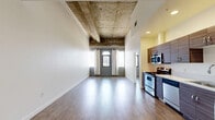 Located on Wilshire Boulevard in the heart of Los Angeles, this 1-bedroom, 1-bathroom unit blends industrial character with modern finishes. The open-plan living and kitchen area is a standout, featuring dramatically exposed concrete beam ceilings that lend an urban loft aesthetic. Wide-plank hardwood-style flooring runs throughout, complementing the clean white walls and creating a warm, cohesive feel. Arched windows allow natural light to fill the living space while framing views of the Los Angeles skyline.

The kitchen is well-appointed with dark wood-grain cabinetry, stainless steel appliances including a range, microwave, dishwasher, and refrigerator, along with an in-unit washer — all integrated into a streamlined galley layout. The bedroom offers a comfortable and private retreat, with arched windows that continue the architectural theme and provide sweeping city views. The room features the same hardwood-style flooring and high ceilings for an airy feel.

The bathroom includes a full soaking tub and shower combo with clean white tile surround. A hallway connects the living areas efficiently, completing this thoughtfully designed urban residence ideal for those seeking modern city living.