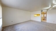 This single-floor residence offers a practical and well-organized layout comprising three bedrooms, two bathrooms, a combined kitchen and living area, and a dedicated closet. The open living room is finished with soft wall-to-wall carpeting and neutral white walls, creating a clean, versatile canvas. A pass-through window connects the living area to the galley-style kitchen, which features warm wood cabinetry, light marble-style countertops, and hardwood-style flooring. White appliances, including a refrigerator and range, are neatly integrated into the kitchen's efficient dual-counter layout.

The bedrooms are carpeted and bright, with several rooms benefiting from windows that allow natural light to filter in. The spacious primary bedroom includes track lighting on the ceiling and a closet with sliding doors. The secondary bedrooms are similarly well-sized with neutral tones and natural light from windows with vertical blinds.

The two bathrooms are practical in design. One features a full tub-and-shower combination with classic beige tile surround and hardwood-style flooring, while the other offers a standalone walk-in shower with tile walls and a sleek glass sliding door. Both bathrooms include wood-toned vanities with light countertops, complementing the consistent warm aesthetic found throughout the home.