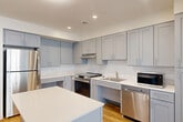 Located in the vibrant Columbia Heights neighborhood of Washington, DC, this thoughtfully designed 2-bedroom, 2-bathroom unit offers a clean, modern aesthetic throughout. Light wood flooring flows seamlessly across the entire space, complementing the bright white walls and creating a warm, cohesive ambiance.

The kitchen is a standout feature, boasting gray shaker-style cabinetry that extends to the ceiling for ample storage, white quartz countertops, a central island ideal for meal prep or casual dining, and a full suite of stainless steel appliances including a refrigerator, range, dishwasher, and microwave. Recessed lighting illuminates the space efficiently.

Each bedroom is comfortably proportioned, featuring large black-framed windows that invite natural light while offering views of the surrounding brick exterior. The rooms maintain a clean, minimalist feel with neutral walls and warm wood flooring.

The two bathrooms are finished in a crisp, contemporary style. One features a soaking tub and a gray vanity with white countertops, while the second is equipped with an accessible roll-in shower complete with grab bars, a fold-down bench seat, and a handheld showerhead. Two dedicated closets provide practical storage throughout the unit.