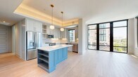 This well-appointed two-bedroom, two-bathroom residence offers a thoughtfully designed single-level layout with contemporary finishes and abundant natural light throughout. The open-concept kitchen and living area serves as the heart of the home, where soft-gray shaker cabinetry, quartz countertops, stainless steel appliances, and a distinctive powder-blue island with built-in shelving create a stylish and functional space. Brass-accented pendant lights and hardware add warm, modern touches. Large floor-to-ceiling windows with sleek black frames flood the living area with natural light and provide open views of the surrounding cityscape.

Light-toned hardwood flooring runs seamlessly through every room, enhancing the bright and airy atmosphere. The spacious primary bedroom features expansive windows on multiple walls, delivering generous natural light and outdoor views. The second bedroom is equally well-lit with large black-framed windows. Both bedrooms are served by dedicated closets, including a walk-in closet with built-in shelving and hanging systems for ample storage.

The bathrooms are finished with elegant marble-style tile, white shaker vanities with gold hardware, pendant lighting, and a soaking tub, reflecting a refined aesthetic. The overall ambiance is clean, modern, and inviting.