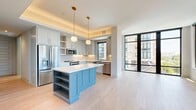 This well-appointed two-bedroom, two-bathroom residence offers a thoughtfully designed single-level layout with contemporary finishes and abundant natural light throughout. The open-concept kitchen and living area serves as the heart of the home, where soft-gray shaker cabinetry, quartz countertops, stainless steel appliances, and a distinctive powder-blue island with built-in shelving create a stylish and functional space. Brass-accented pendant lights and hardware add warm, modern touches. Large floor-to-ceiling windows with sleek black frames flood the living area with natural light and provide open views of the surrounding cityscape.

Light-toned hardwood flooring runs seamlessly through every room, enhancing the bright and airy atmosphere. The spacious primary bedroom features expansive windows on multiple walls, delivering generous natural light and outdoor views. The second bedroom is equally well-lit with large black-framed windows. Both bedrooms are served by dedicated closets, including a walk-in closet with built-in shelving and hanging systems for ample storage.

The bathrooms are finished with elegant marble-style tile, white shaker vanities with gold hardware, pendant lighting, and a soaking tub, reflecting a refined aesthetic. The overall ambiance is clean, modern, and inviting.
