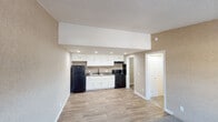 This single-floor residence at 3428 Marabou Mills Dr in Indianapolis, Indiana, offers a straightforward, functional layout with distinct living, sleeping, and kitchen zones. The living area greets occupants at the front entry, where a large window allows natural light to fill the carpeted space, transitioning seamlessly to wood-look hard flooring that extends into the kitchen. The kitchen is designed with practicality in mind, featuring an abundance of white cabinetry providing generous storage, dark granite-style countertops, a double-basin sink, and a full suite of black appliances including a refrigerator, electric range, and range hood, all illuminated by recessed lighting. A hallway connects the main living space to the private areas of the unit. The bedroom is comfortably sized, with plush carpeting, a ceiling fan with light fixture, and a window that brings in outside views and natural light. The bathroom is well-appointed with wood-look flooring, a granite-topped vanity with a distinctive glass bowl sink, a framed mirror, and a full tub-shower combination with chrome fixtures. Textured walls and popcorn ceilings are consistent throughout the space, contributing to its cohesive, understated aesthetic.
