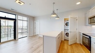 Located at 300 E Fifth Ave in Columbus, Ohio, this single-floor residence showcases a clean, modern design with an open and airy feel throughout. Light hardwood flooring runs continuously across the living spaces, complementing a neutral, bright color palette that enhances the sense of openness.

The kitchen is a standout feature, outfitted with white shaker-style cabinetry extending to the ceiling, a white subway tile backsplash, quartz countertops, and a full suite of stainless steel appliances including a refrigerator, range, microwave, and dishwasher. A central island with pendant lighting provides additional prep space and anchors the open-concept layout. A stacked washer and dryer unit is conveniently tucked behind louvered doors just off the kitchen.

The bedroom is generously proportioned with large windows offering outdoor views and ample natural light, accompanied by a dedicated closet with built-in shelving. The hallway features a recessed electrical panel and connects the rooms efficiently.

The bathroom is thoughtfully designed with a frameless glass walk-in shower clad in vertical white tile, matte black hardware accents, and wood-toned flooring. A second full bathroom includes a shaker-style vanity, an arched mirror, and matte black fixtures, maintaining a cohesive modern aesthetic. This residence offers a well-appointed, contemporary living environment in the heart of Columbus.