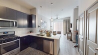 This contemporary single-floor residence offers a thoughtfully designed open-concept layout that seamlessly connects the kitchen, dining, and living areas. The kitchen is a standout feature, outfitted with dark flat-panel cabinetry, a crisp white subway tile backsplash, a generous peninsula with light quartz countertops, pendant lighting, and a full suite of stainless steel appliances including a gas range, microwave, refrigerator with ice maker, and dishwasher. Light wood-style flooring runs throughout the main living areas, enhancing the bright and airy atmosphere. The living room benefits from a large sliding glass door that invites abundant natural light, complemented by a ceiling fan overhead. The bedroom is a tranquil retreat with plush carpeting, large windows dressed with horizontal blinds and patterned drapes, and ample natural light. The bathroom features wood-tone cabinetry, a white quartz vanity countertop, a backlit mirror, light wood-style flooring, and direct access to a walk-in closet with built-in shelving. Throughout the space, neutral tones and clean lines create a cohesive, modern aesthetic that is both functional and visually refined.