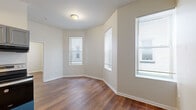 This efficiently designed 2-bedroom, 1-bathroom unit offers a practical and well-appointed layout across a single floor. Warm-toned wood-look flooring runs consistently throughout the space, complementing the neutral, light-colored walls that lend a clean and cohesive aesthetic.

The living area benefits from multiple windows dressed with horizontal blinds, allowing natural light to filter in and creating an open, airy feel despite the compact footprint. Notably elevated ceilings in portions of the living area add a sense of verticality to the space.

The kitchen is efficiently equipped with gray cabinetry, granite-style countertops, a stainless steel range, a black refrigerator, and an under-cabinet range hood — offering all essential cooking amenities in a tidy, functional arrangement.

The primary bedroom features multiple windows that bring in ample daylight, while the second bedroom, though more intimate in scale, includes a window and direct access to a closet. An additional area off the primary bedroom provides access to both a closet with a hanging rod and a separate room, adding useful storage options.

The bathroom is finished with large-format gray tile on both the floor and tub surround, a built-in shower niche, and a combination tub and shower — delivering a polished, modern look.