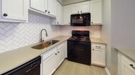 This contemporary apartment offers a blend of comfort and style. The open floor plan maximizes space, with wood-style flooring throughout creating a cohesive look. Large windows in the living areas provide ample natural light, enhancing the sense of spaciousness. The kitchen boasts white cabinetry, black appliances, and a striking herringbone backsplash. The bathroom features a clean, white design with a shower-tub combination. Neutral wall colors and textured ceilings contribute to a fresh, modern aesthetic. The apartment's layout includes multiple rooms, offering versatility for various living arrangements.